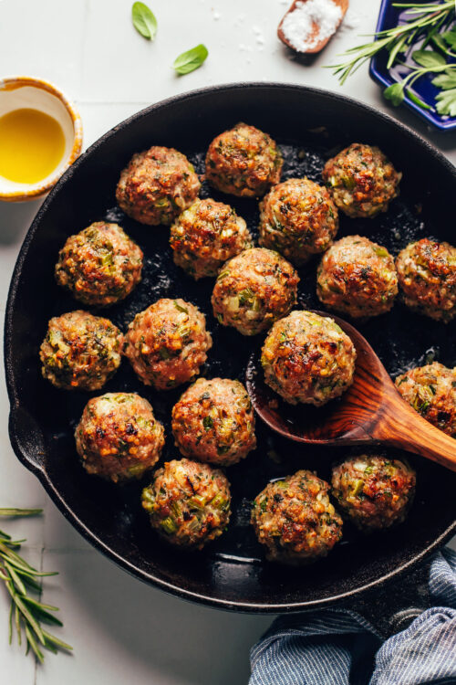 Spoon holding a turkey meatball in a cast iron skillet of more meatballs