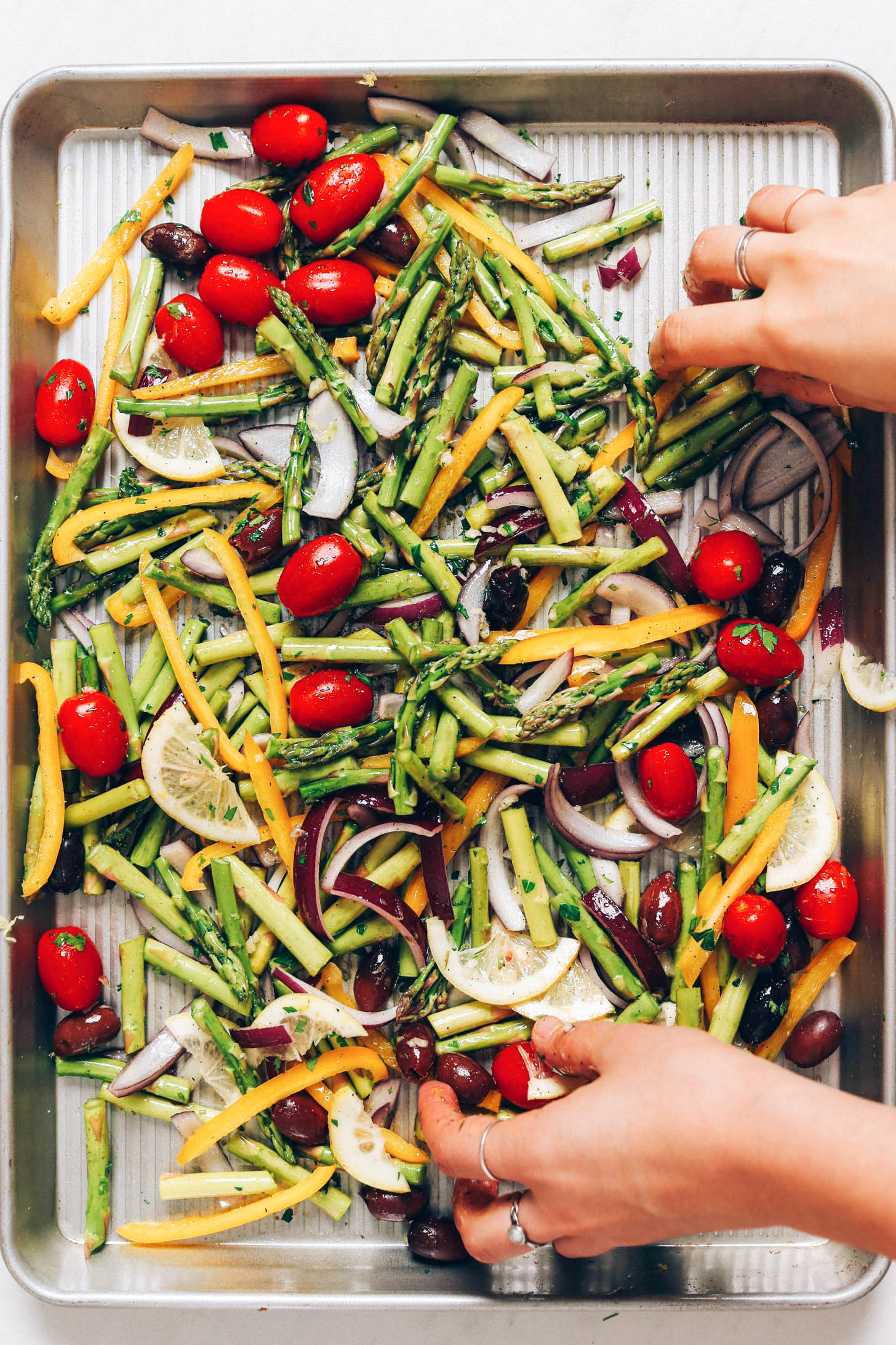 Tossing asparagus, cherry tomatoes, onion, bell pepper, and olives with parsley, lemon, and olive oil