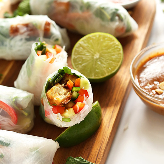 Sliced open Tofu Vietnamese Spring Roll on a cutting board with limes and more rolls
